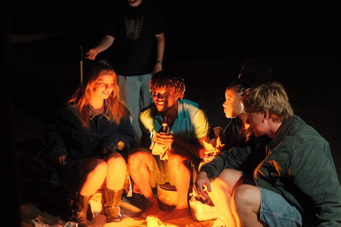 Cast gathered around a bonfire at night on set
