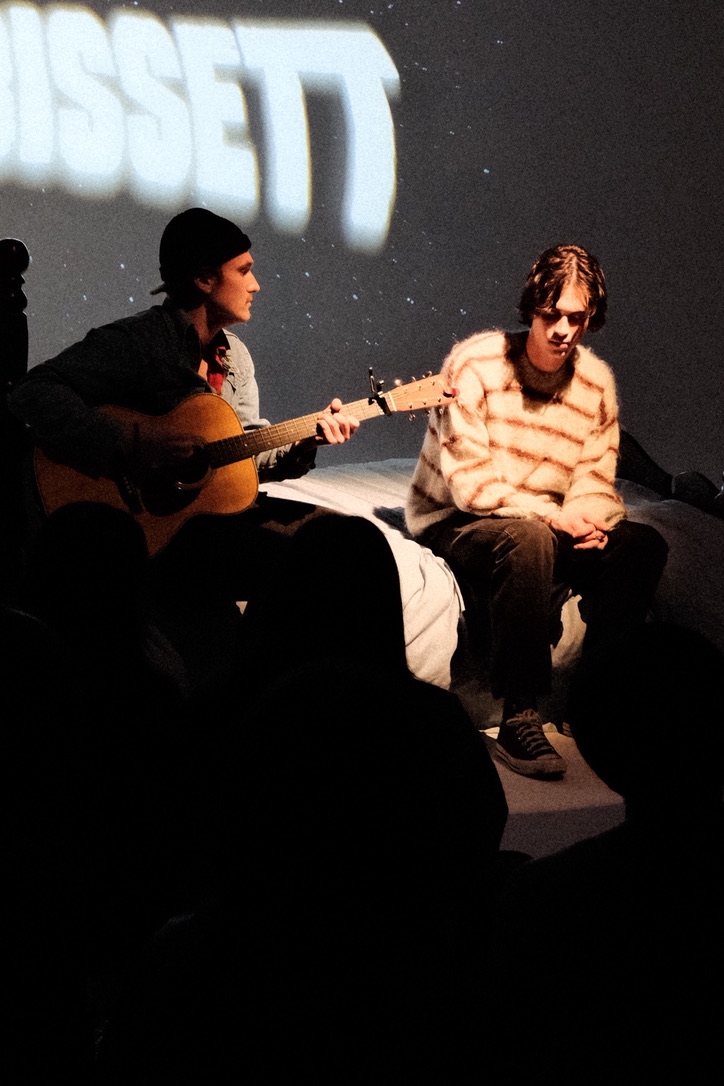 Two performers on stage with name projected behind them