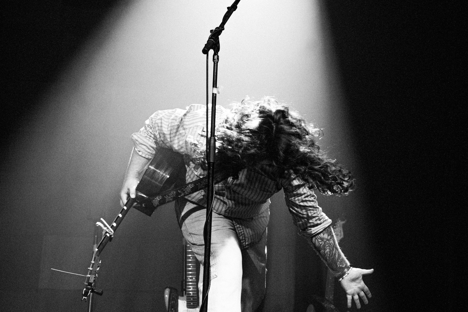 Guitarist bent forward under a spotlight, hair flying, black and white