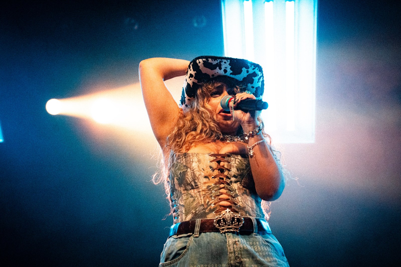 Singer in a cow-print cowboy hat at the microphone, blue stage light