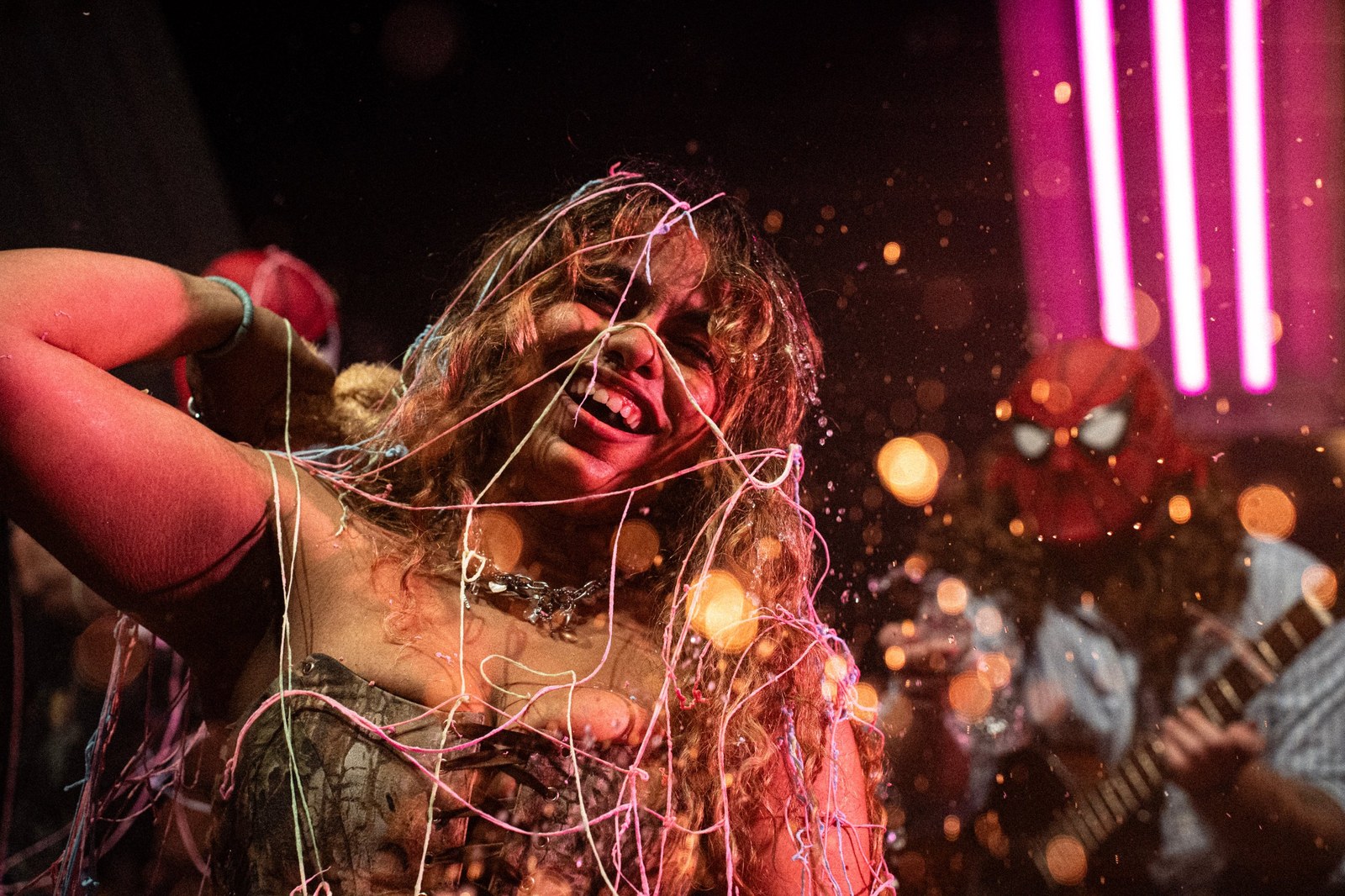 Singer laughing, covered in silly string, under pink stage lights