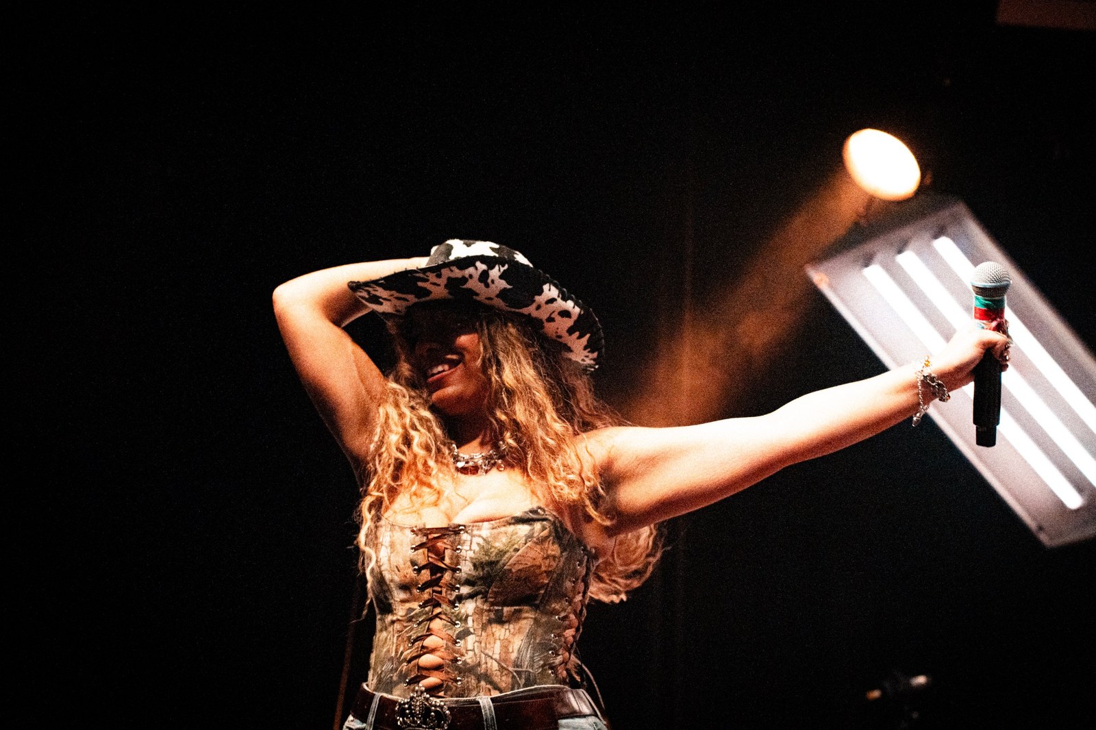 Singer in a cowboy hat holding the microphone out at arm's length