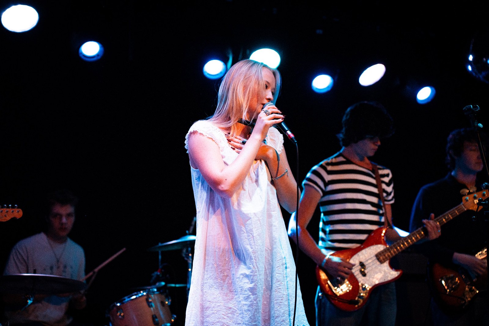 Singer with a hand on her chest at the mic, band playing behind her