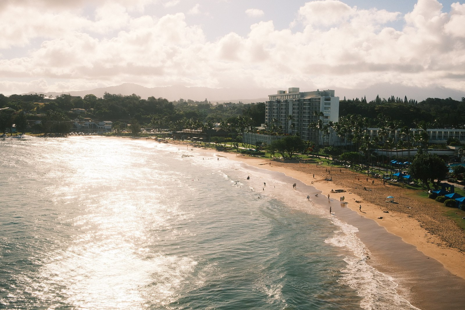 Sunlit beach and hotel seen from above, waves rolling in