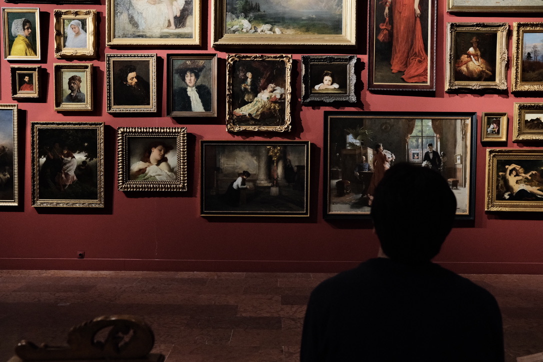 Silhouette of a visitor viewing a gallery wall of paintings